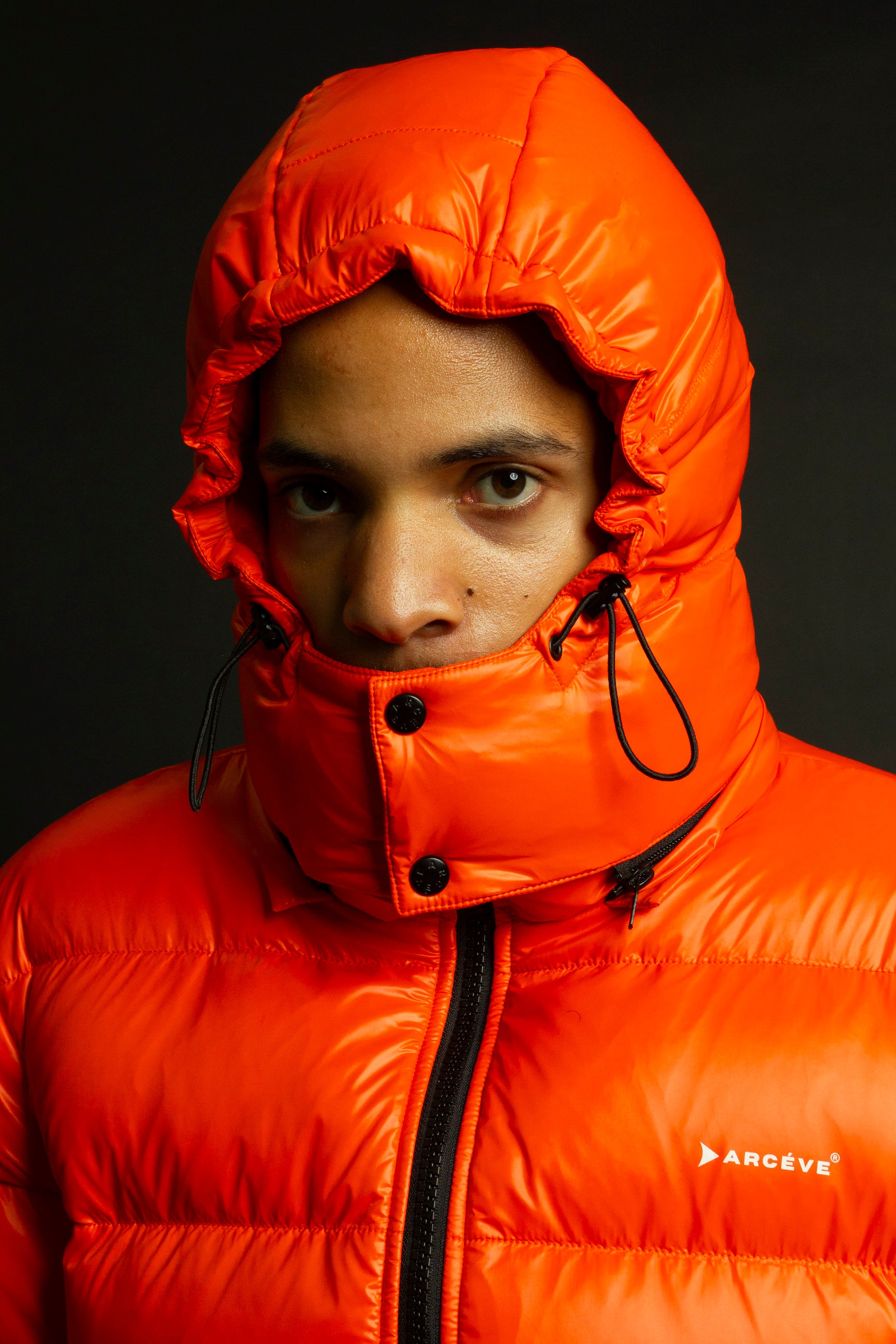 ARCÉVE The Mont Jacket - Close-up of the signature ARCÉVE logo on the chest hooded down jacket - Orange
